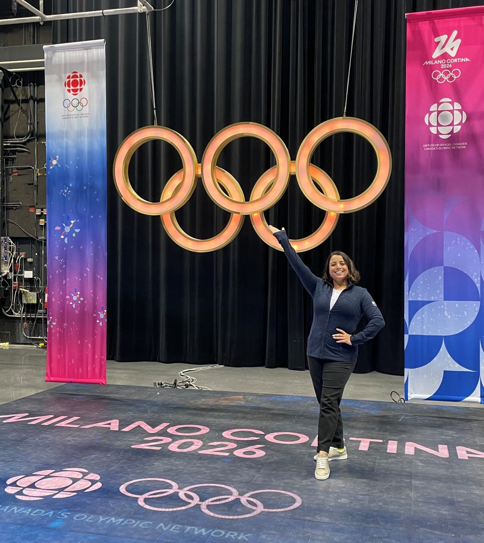 A person stands in front of the Olympic rings and poses for the camera.