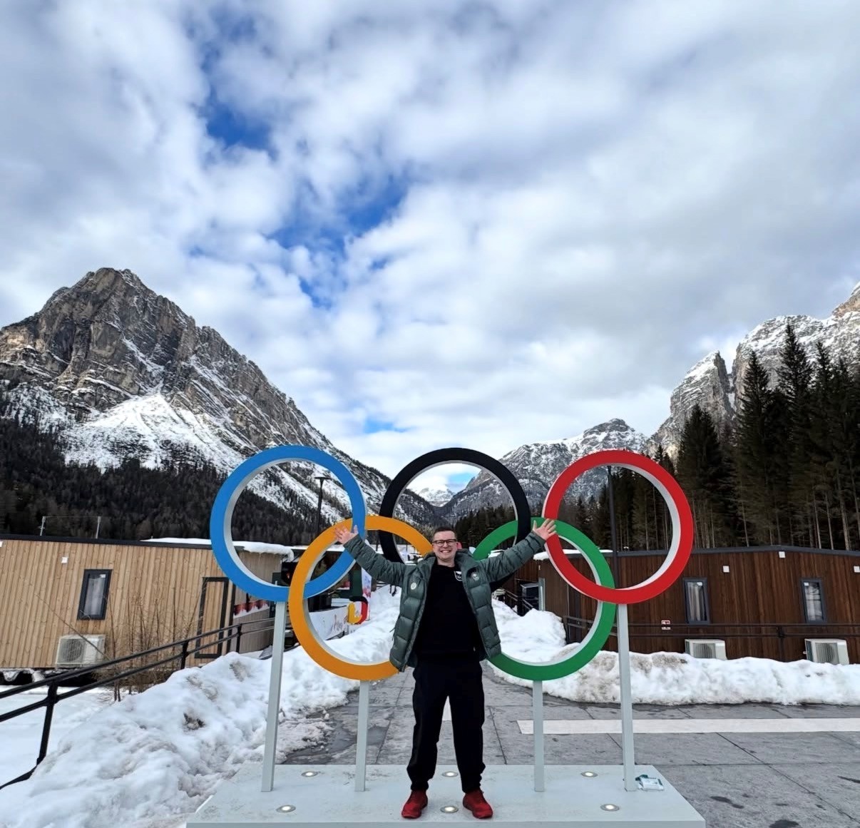 A person stands outside in front of the Olympic rings with their arms raised
