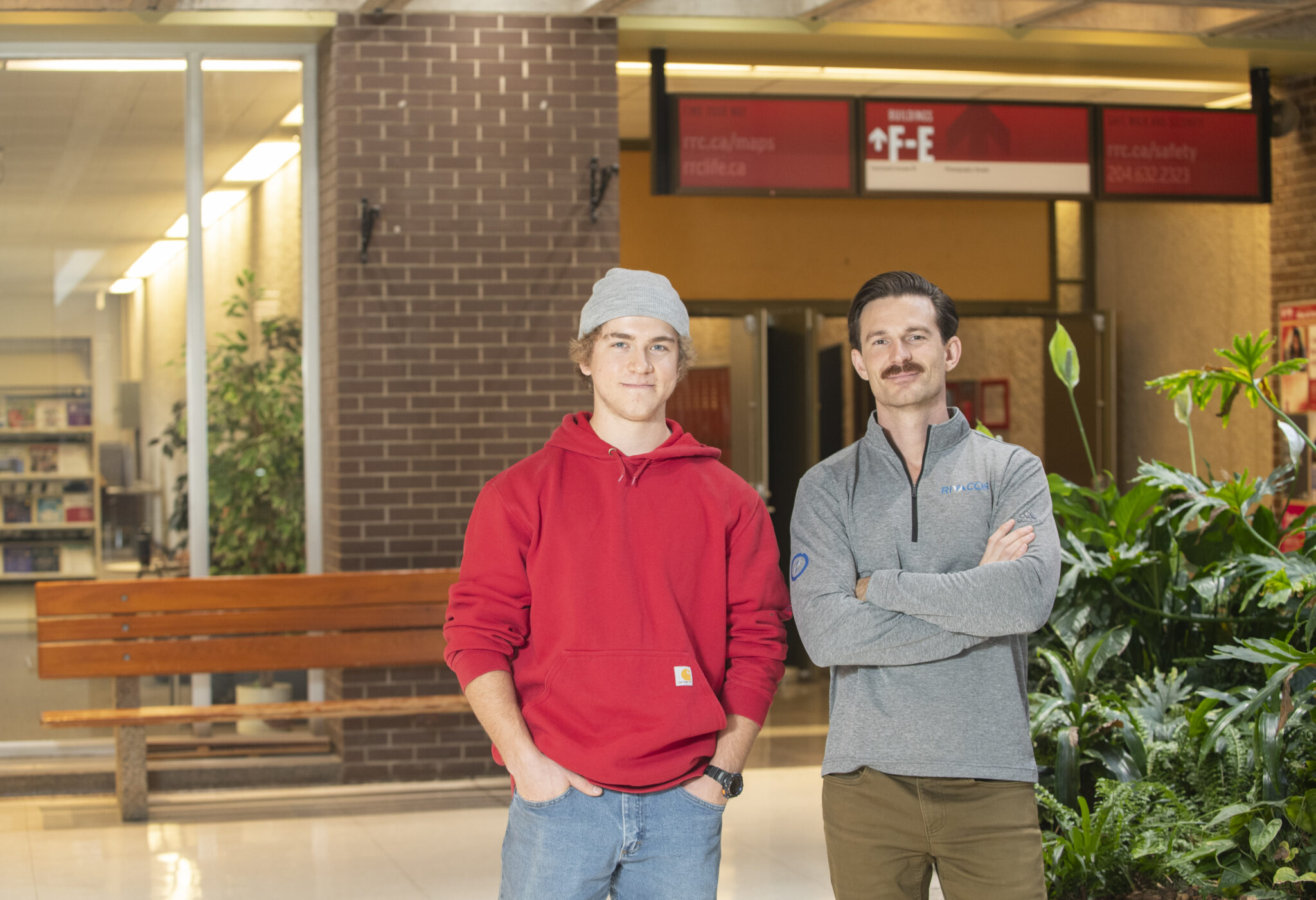 Two men stand in a hallway at the Notre Dame campus of RRC Polytech. They are both smiling.