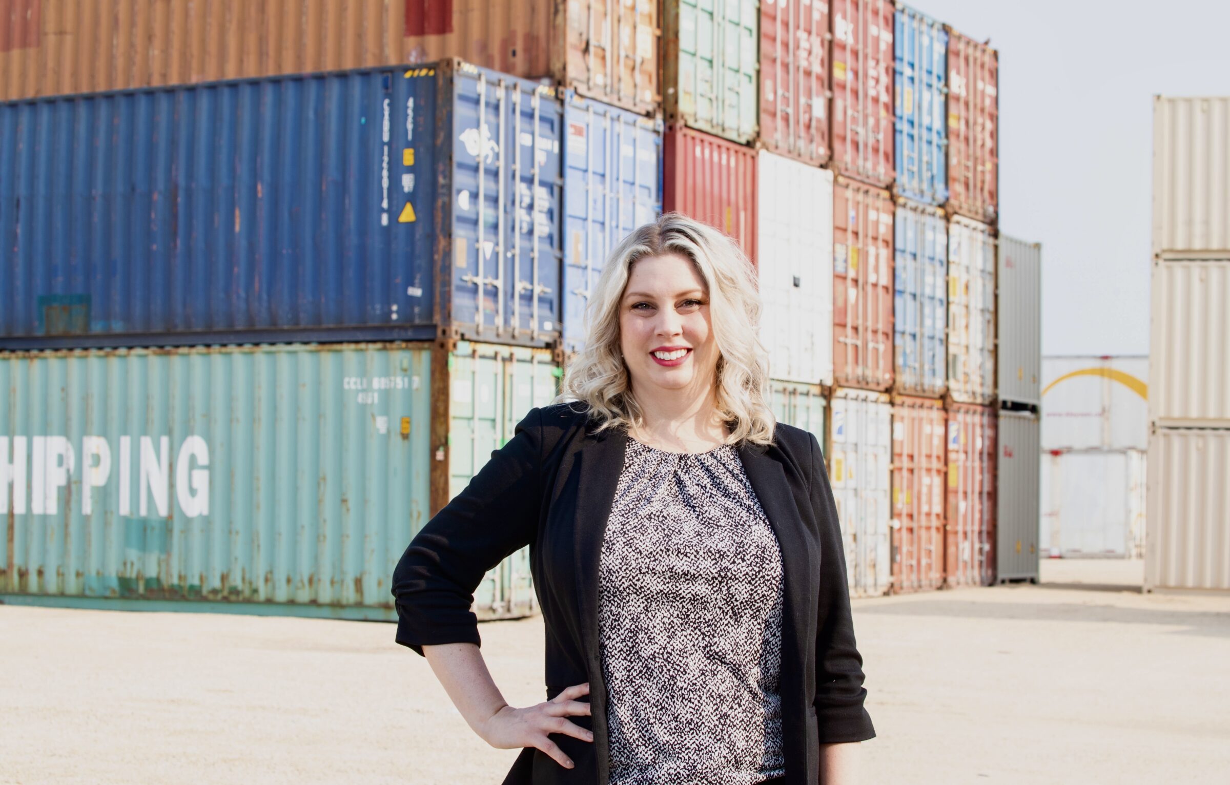 Carly Edmundson, a woman with blonde hair is standing in front of shipping containers.