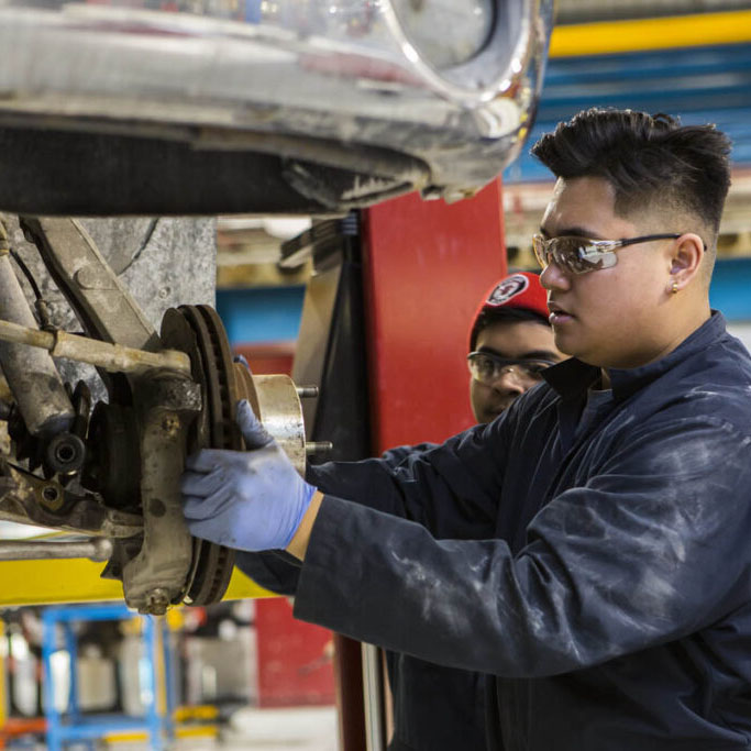 Two automotive students working on a vehicle in a shop. 