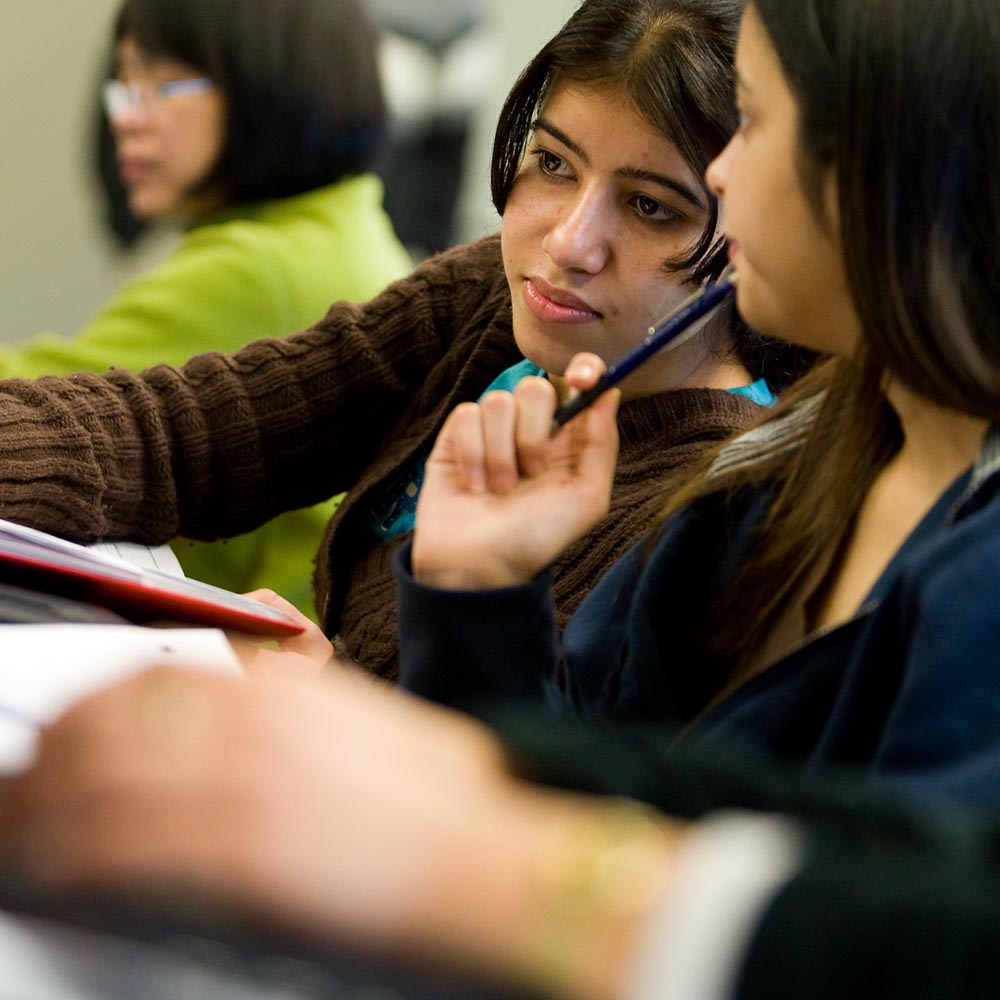 Two students talking with each other and exchanging notes.