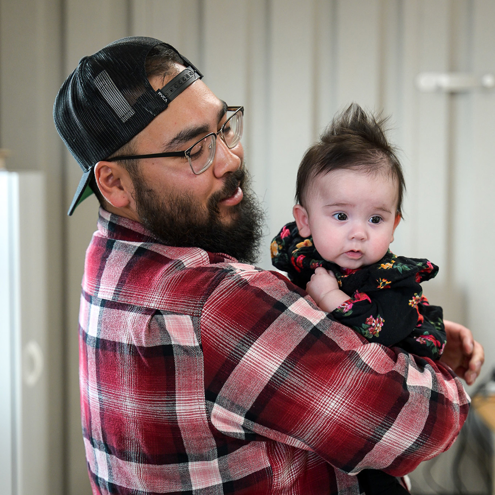 A father with his hat on backwards holding his baby daughter. 