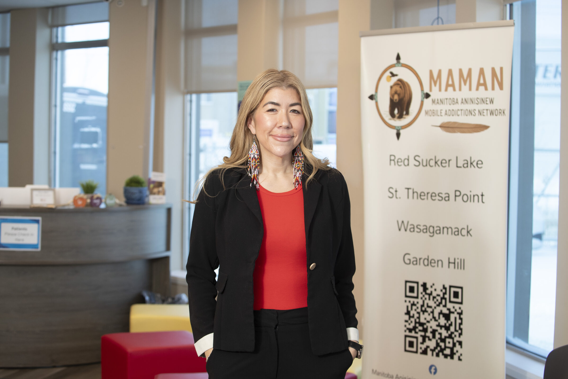 RRC Polytech grad Kirsty Muller wears a black blazer and red top, with long, beaded earrings.