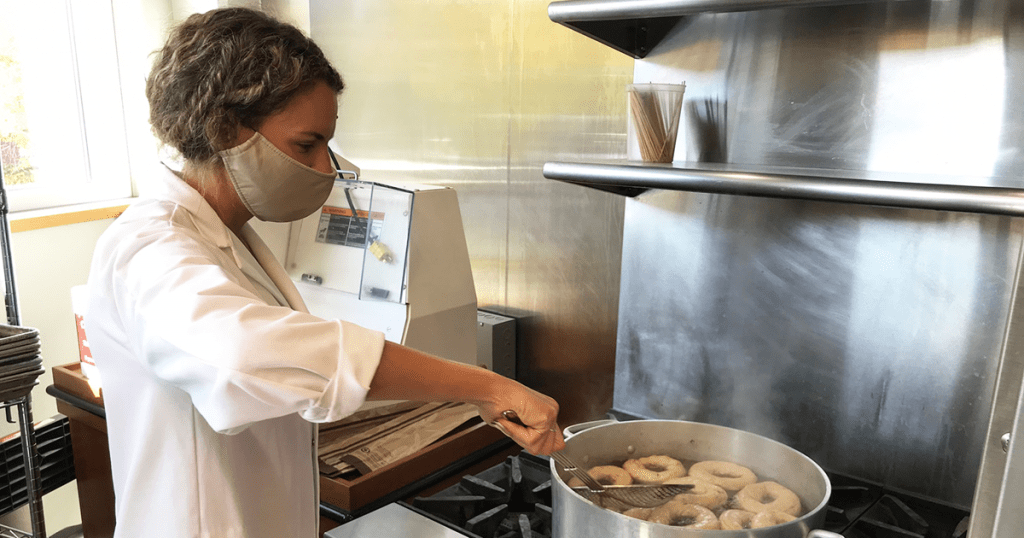 Woman wearing face mask in commercial kitchen boiling bagels