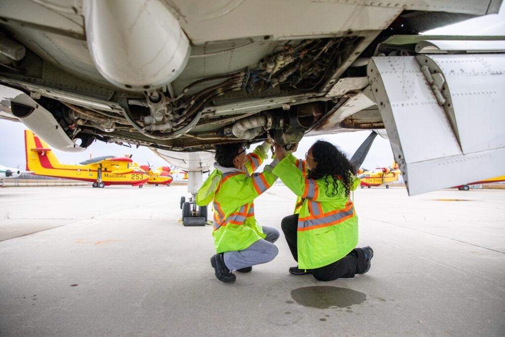 two people in safety gear crouched under an aircraft