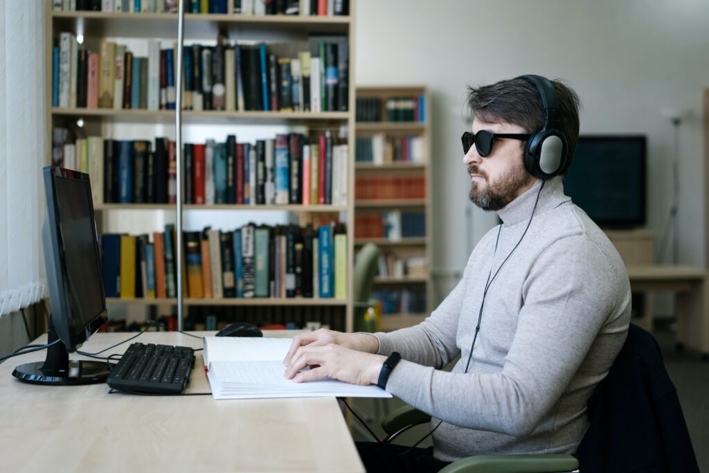Picture of a blind person using braille and wearing a headset connected to a computer