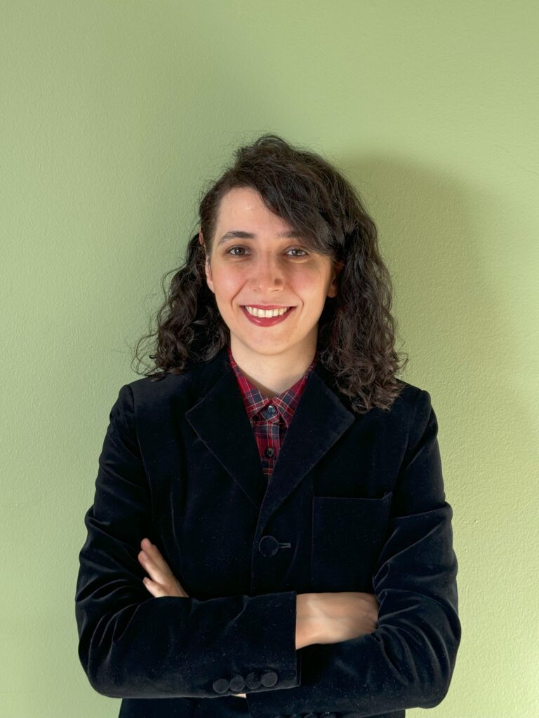 A woman in a blazer stands with her arms crossed and smiles at the camera.