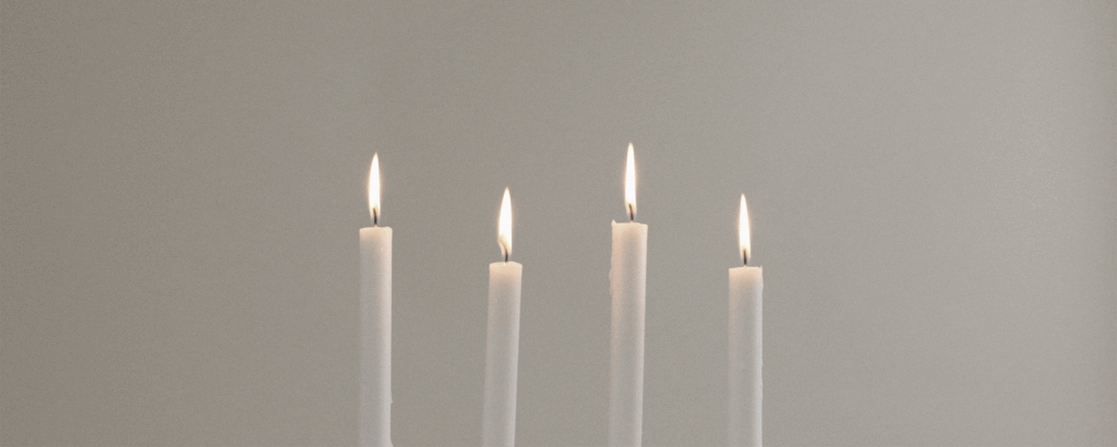 Four lit candles on a plain backgroung