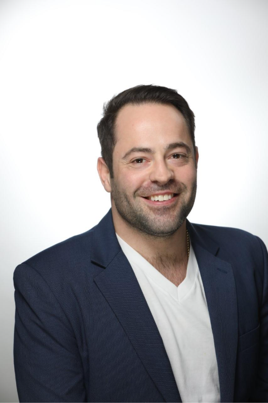 A person wearing a blue blazer smiles at the camera.