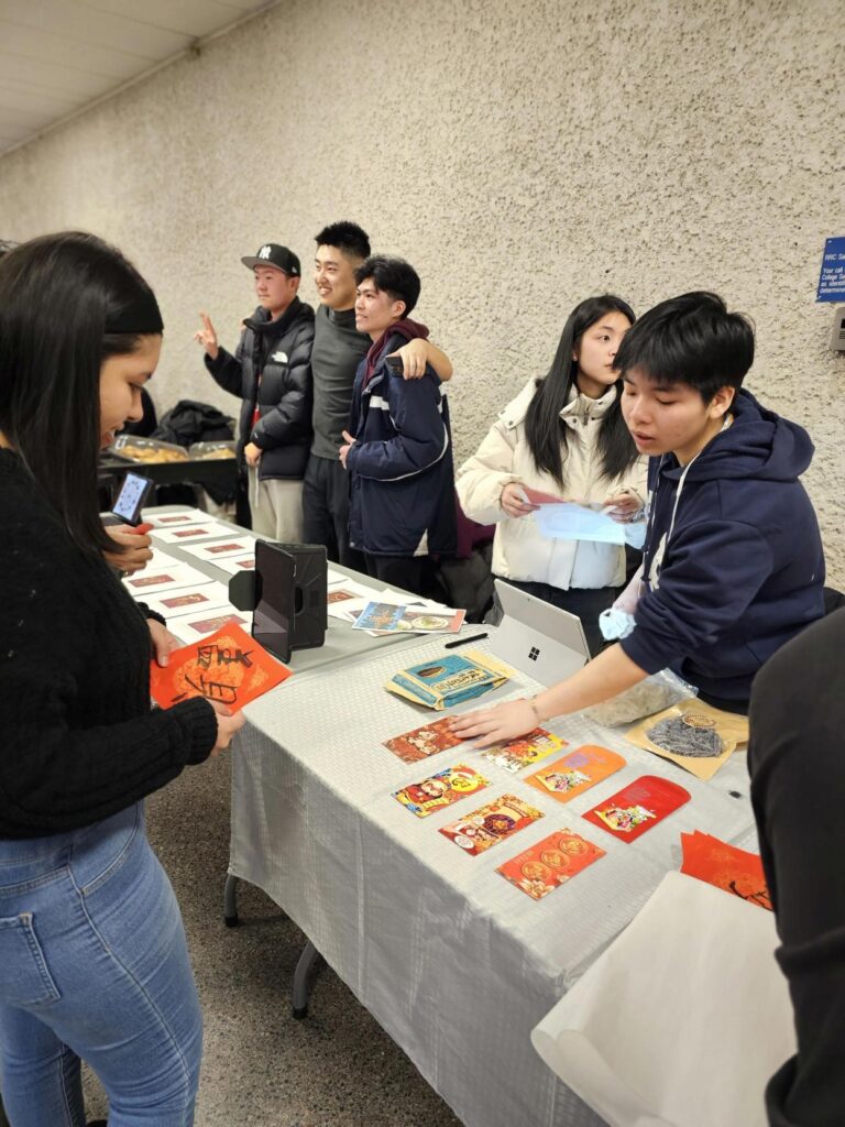 People gathered at a table displaying red cards and cultural materials during a campus event