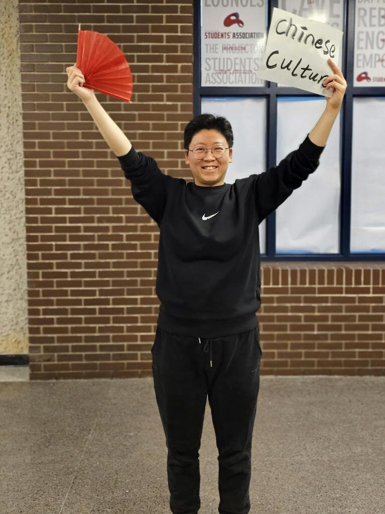 Person holding a red fan and a sign that reads “Chinese Culture” in a hallway.