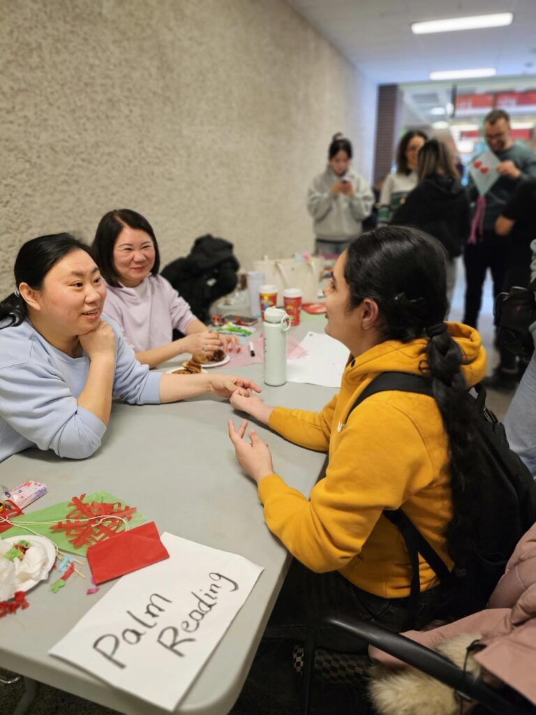 People seated at a table participating in a palm reading activity during a campus event.