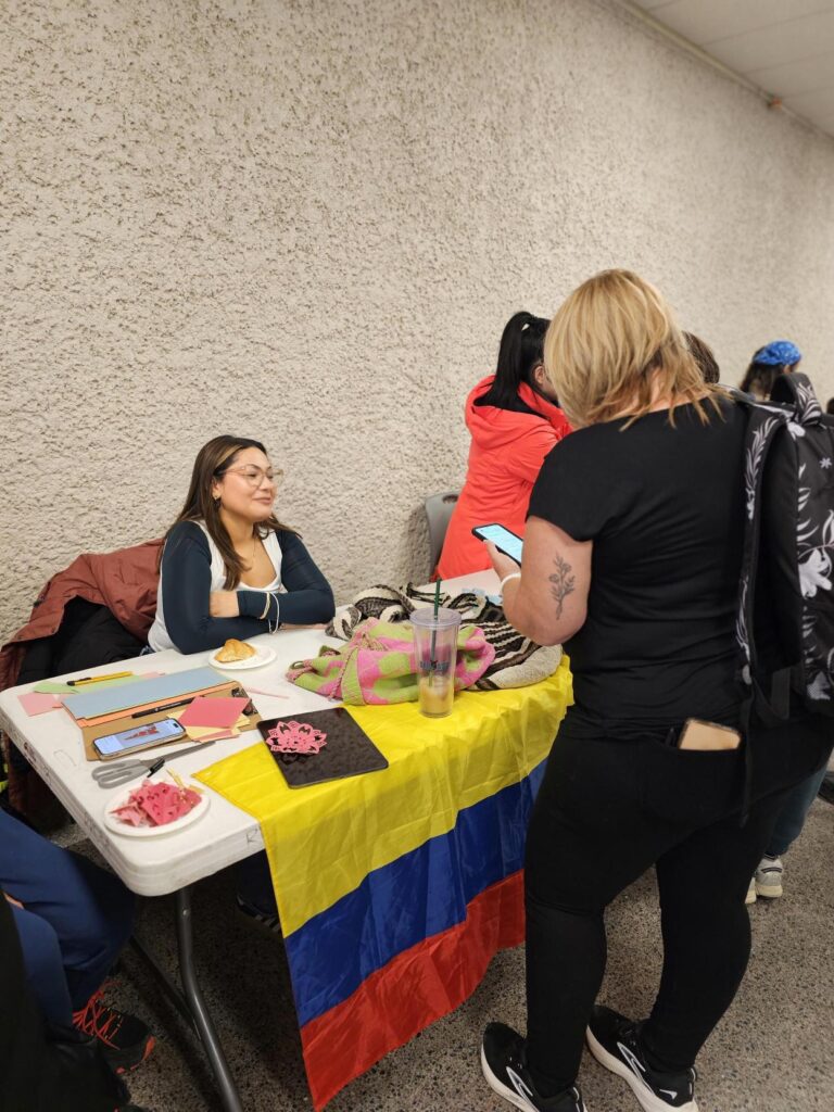 A person seated behind a table decorated with a Colombian flag and crafts.