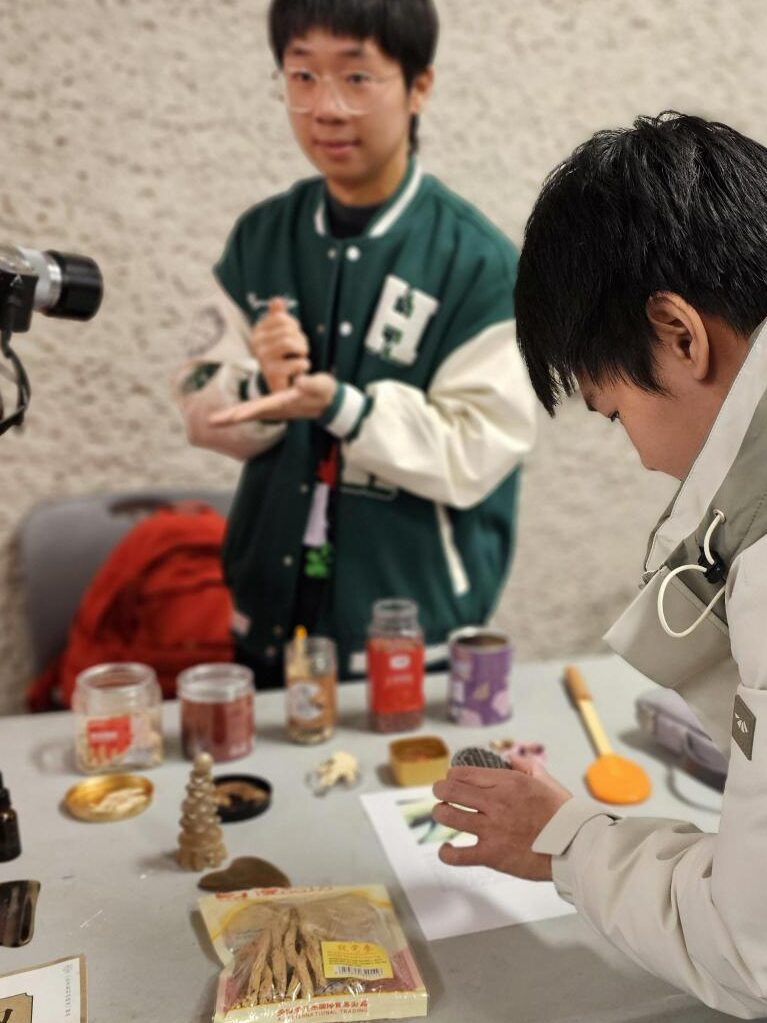 People examining herbs and traditional items at a cultural display table.