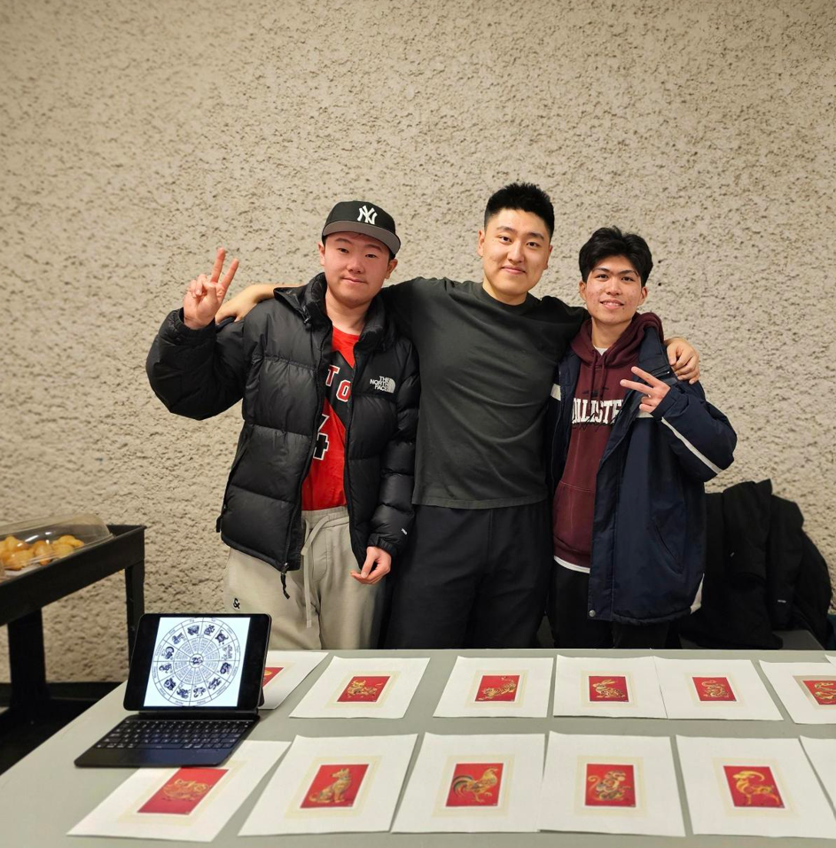Three people posing behind a table displaying red greeting cards and a laptop.