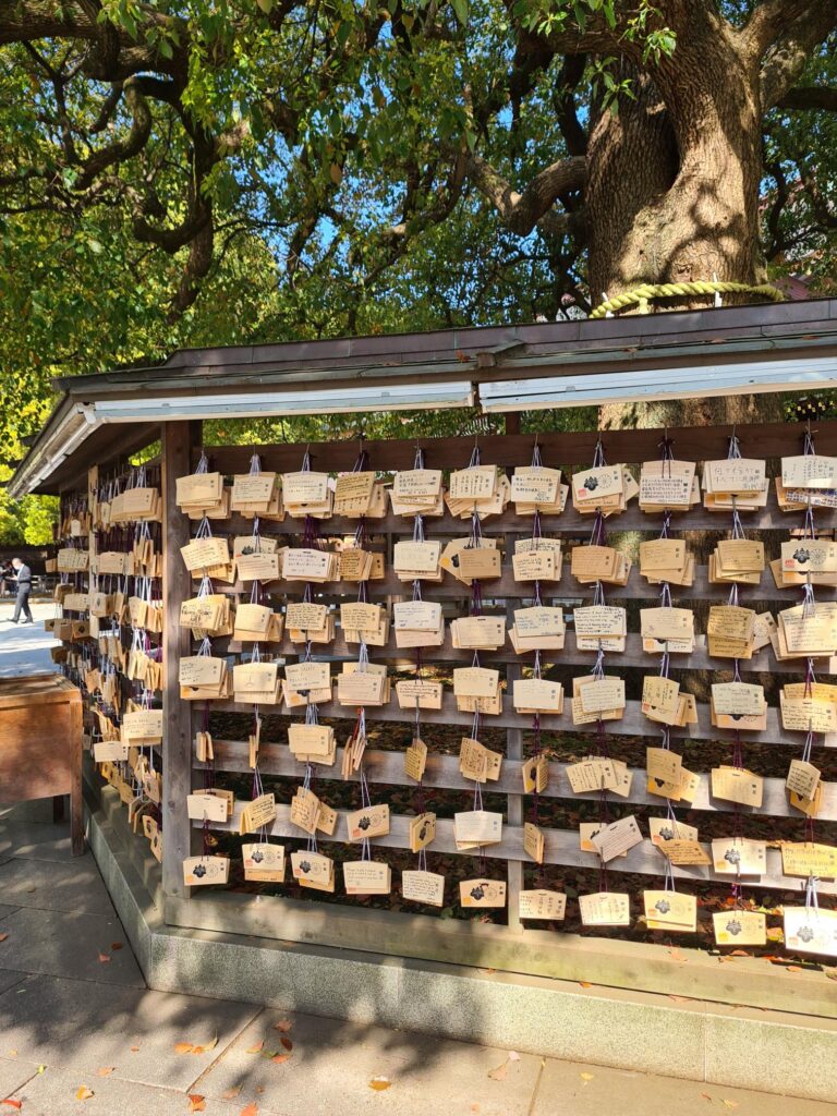 Wooden wall covered with hundreds of small rectangular plaques, each tied with string, arranged in neat rows outdoors.
