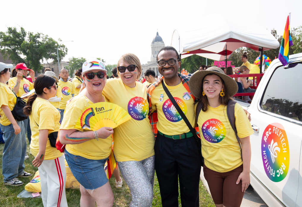 Four people wearing yellow RRC Polytech Pride t-shirts stand together outdoors near a decorated vehicle, with others in matching shirts gathered behind them during a Pride event.