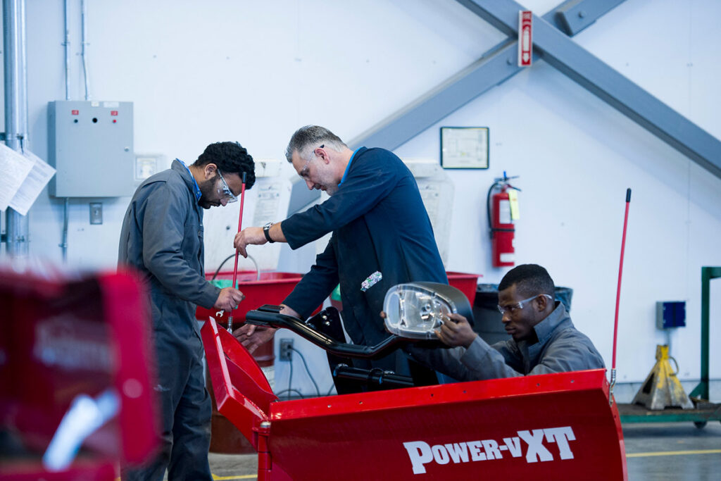 Instructor showing students how to do something on a vehicle in a machine shop