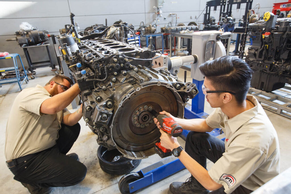 Students working on a large vehicle engine in a shop