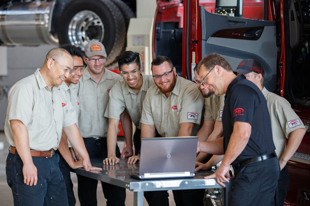 Students and instructor gathered around a laptop in a heavy equipment shop