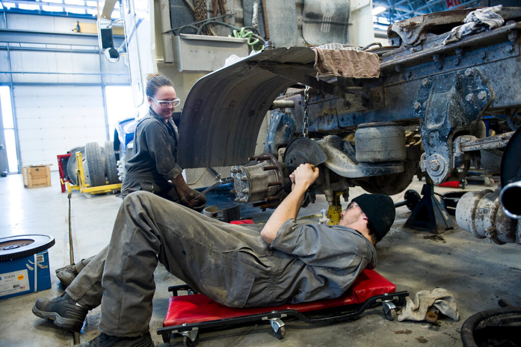 Automotive students working on the wheel of a large vehicle in a shop