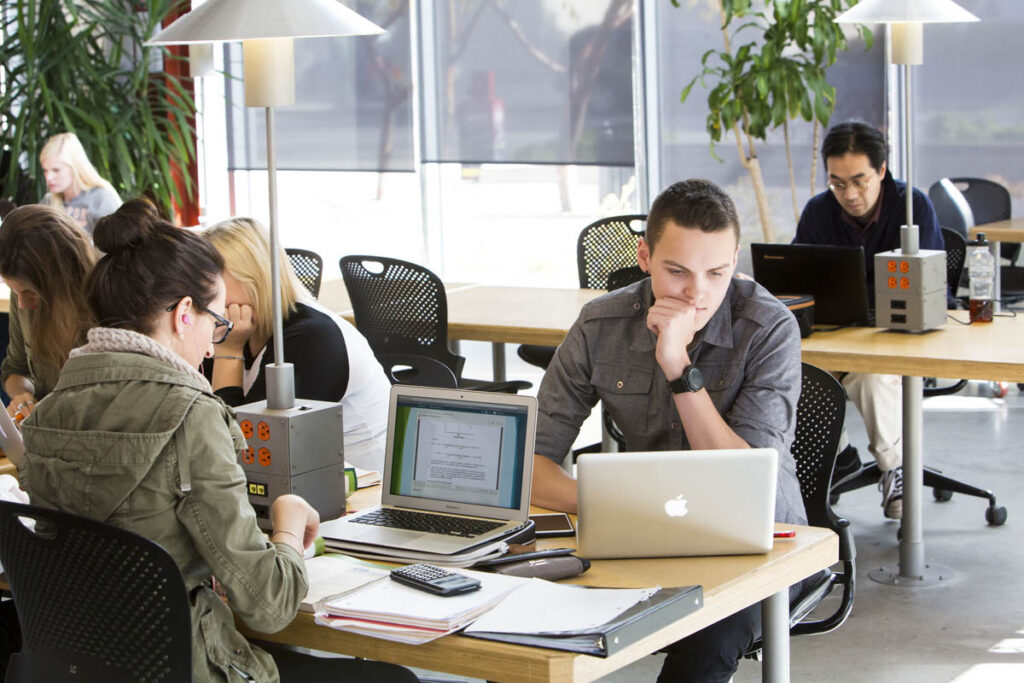 Two students working on laptops in an open workspace 