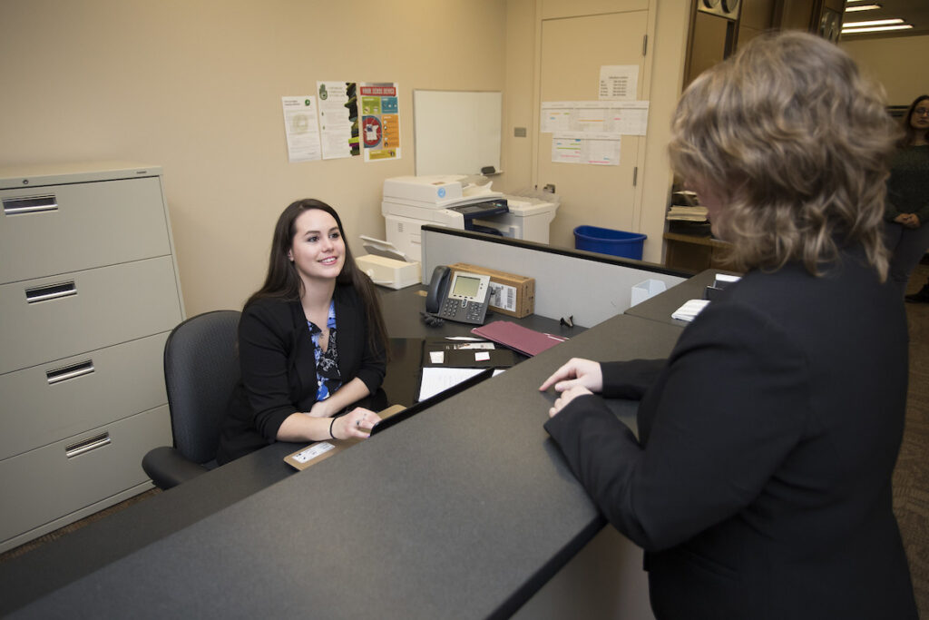Administrative assistant talking to person at desk in an office
