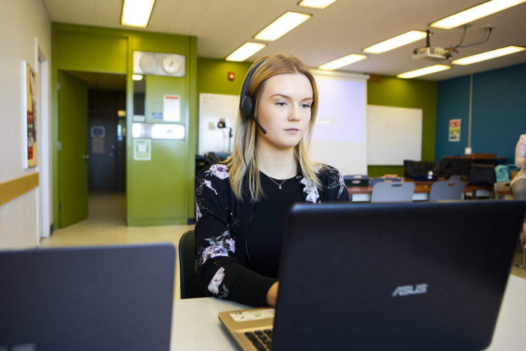 Student with headset on working on a laptop in a classroom