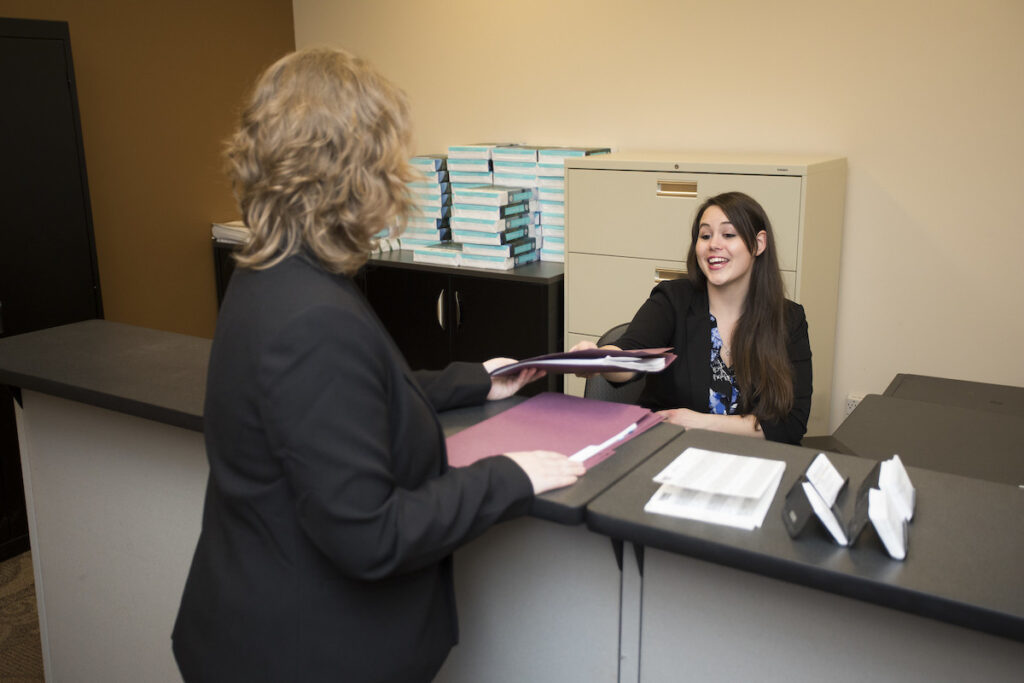 Administrative assistant talking to person at desk in an office