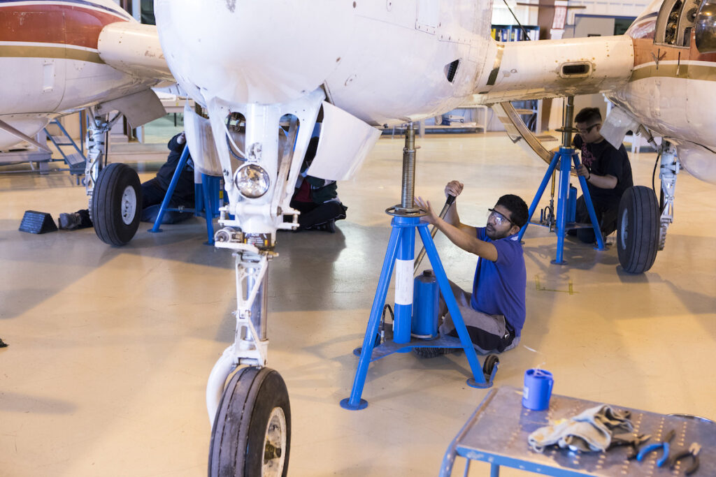Student working on the underside of an aircraft in a hangar 
