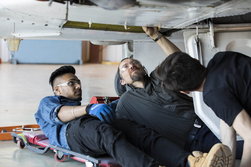 Two students working on the underside of an aircraft in a hangar 