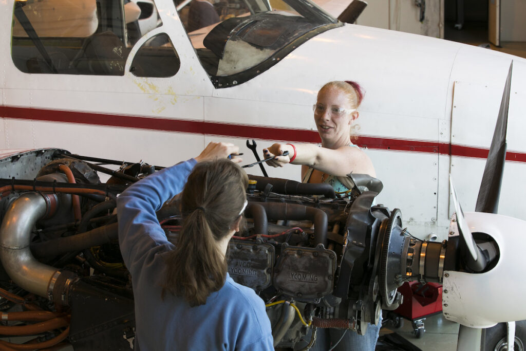 Two students working on an aircraft propeller in a hangar