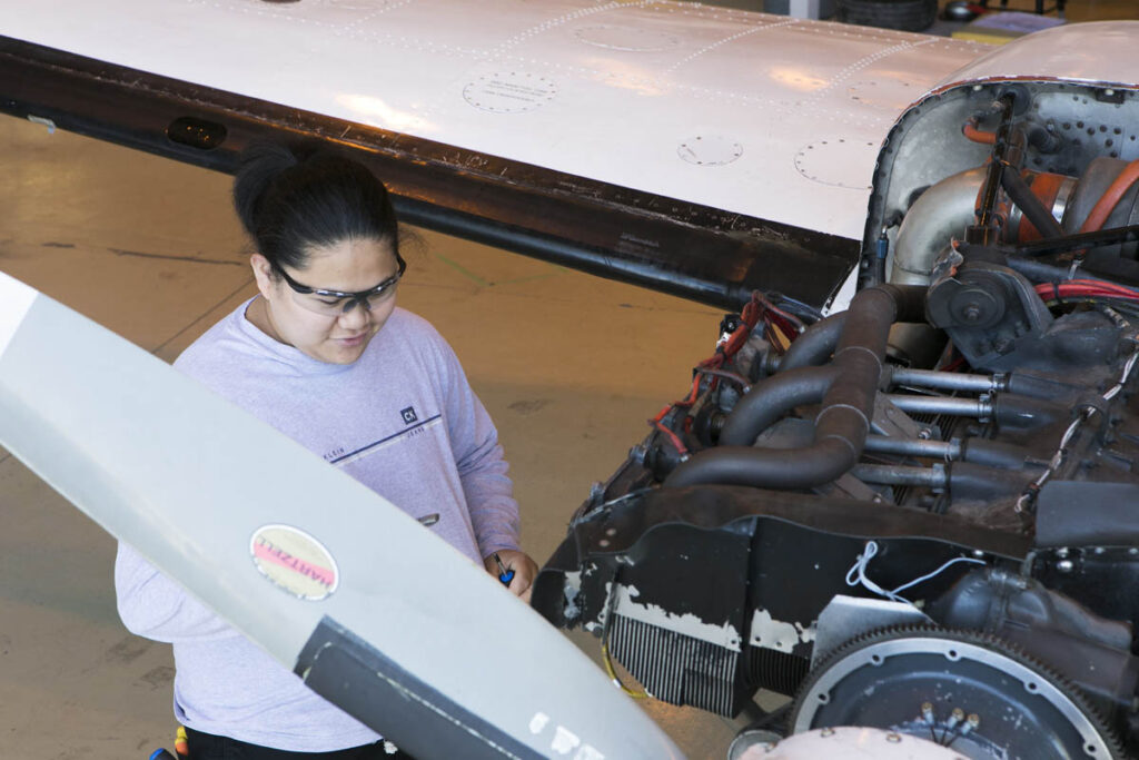 Student inspecting the engine of an airplane in a hangar