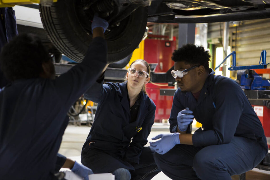 Two automotive students working on a vehicle's tire in a shop