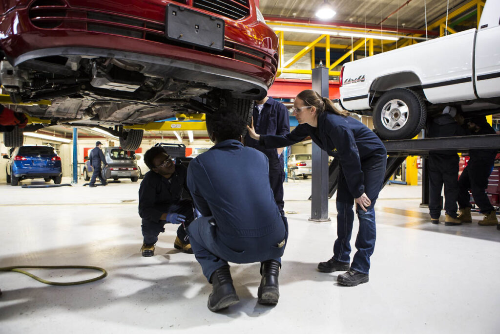 Three automotive students working on a vehicle's tire in a shop