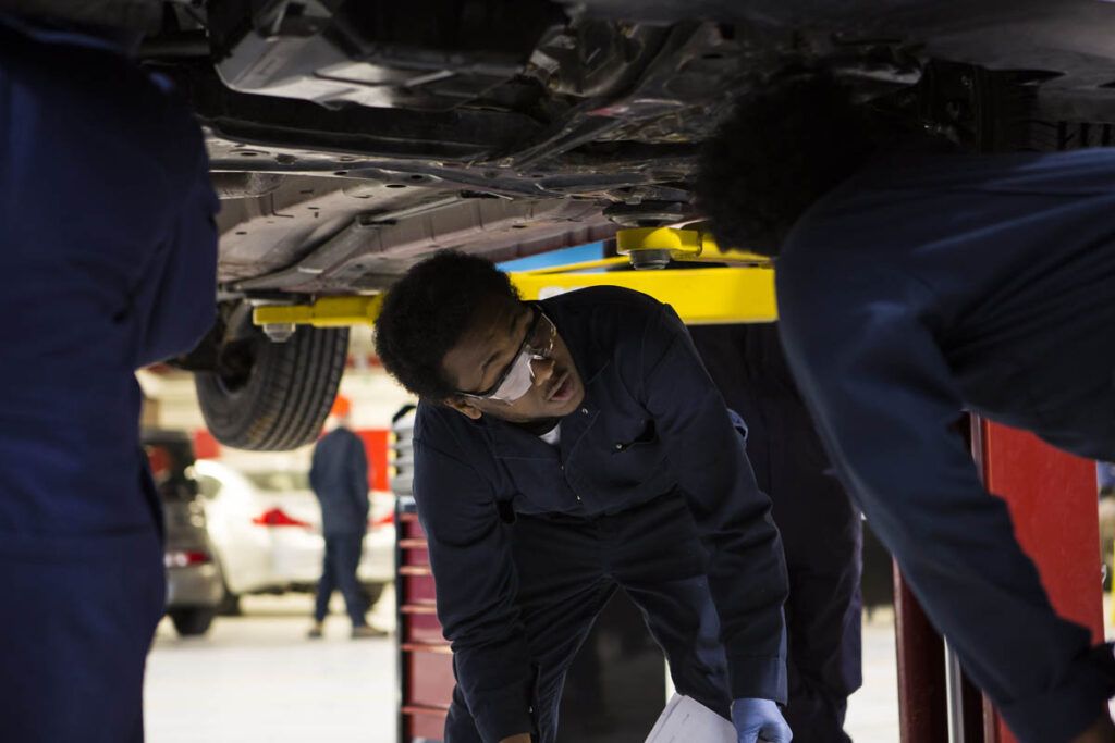 Automotive students working underneath a raised up vehicle in a shop