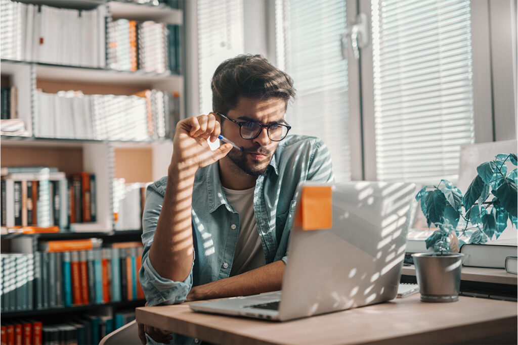 Man at a table in a home office looking at his laptop screen