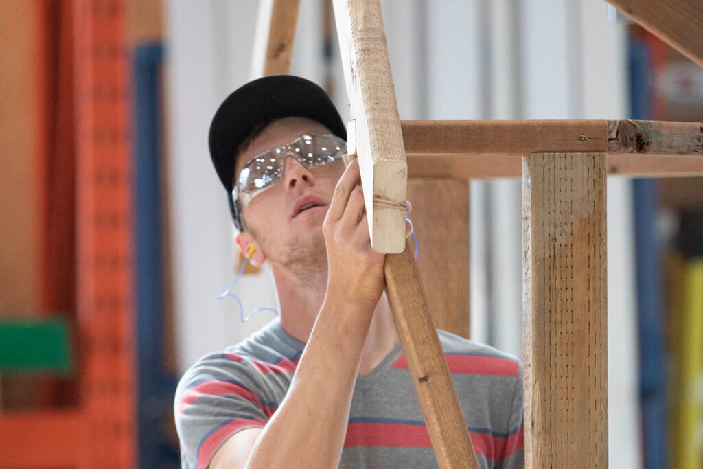 Carpentry student living up piece of wood while framing a structure