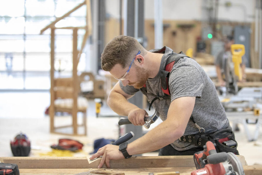 Carpentry student holding a hammer and working with a piece of wood in a carpentry shop