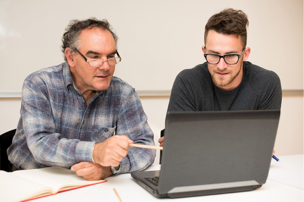 Instructor and student in a classroom looking at a laptop