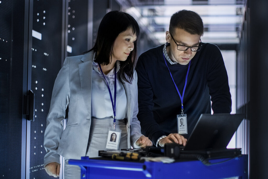 Two networking technicians working on a laptop in a networking room