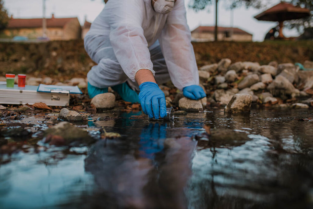 Person in hazmat suit collecting water samples from stream