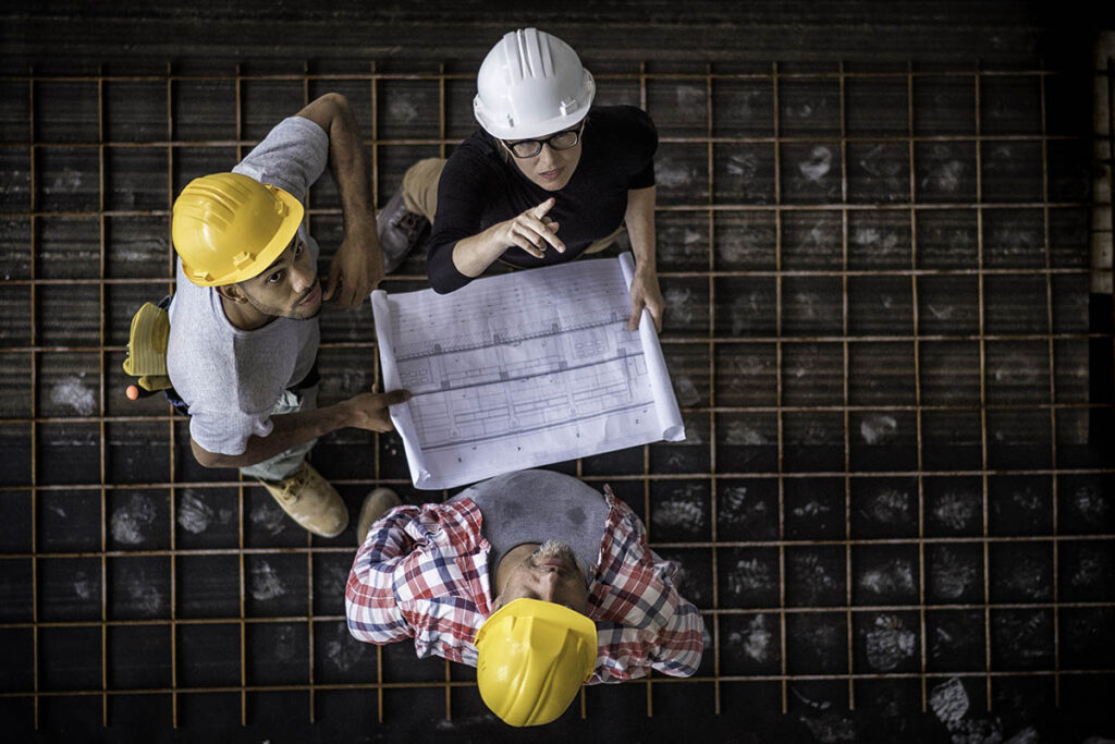 Birdseye view of three people in hard hats talking to each other while looking at blueprints