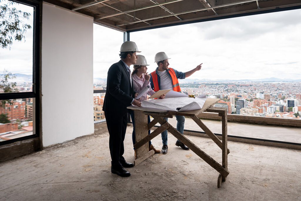 Three people with suits and hard hats at a construction site overlooking a city