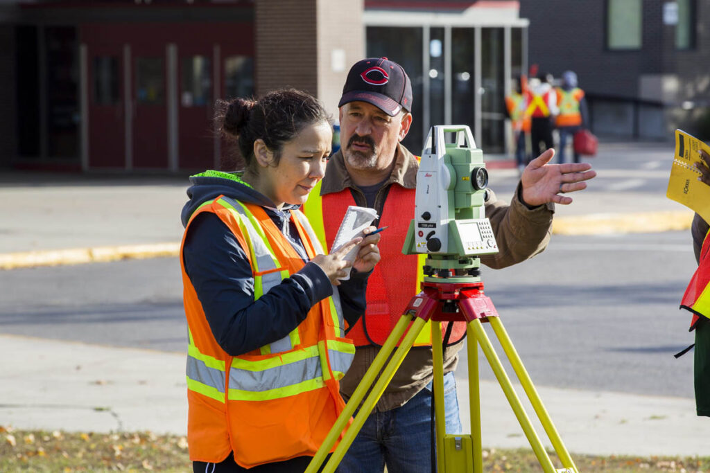Instructor showing civil technician student how to use surveying equipment