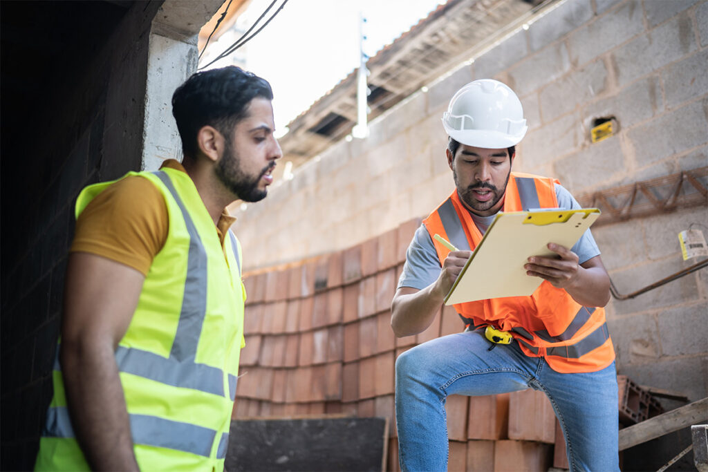Two people wearing safety vests looking at notes at a construction site