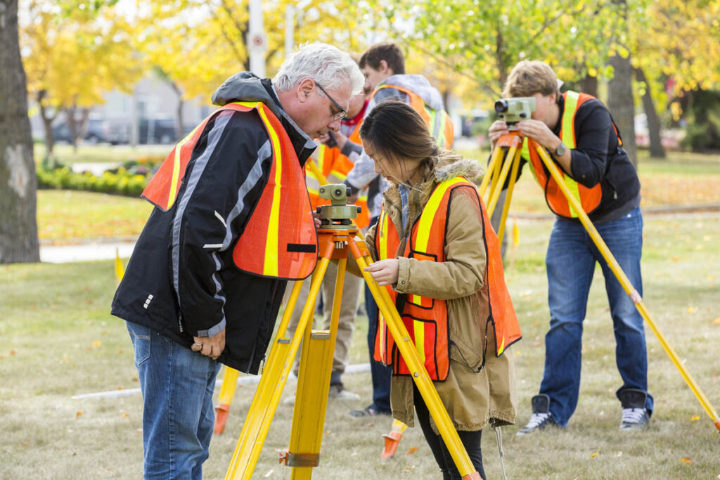 Civil technician student surveying outdoors while instructor watches on