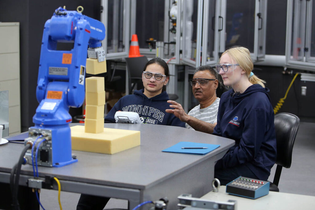 Students watching a robotic arm stack blocks in a lab