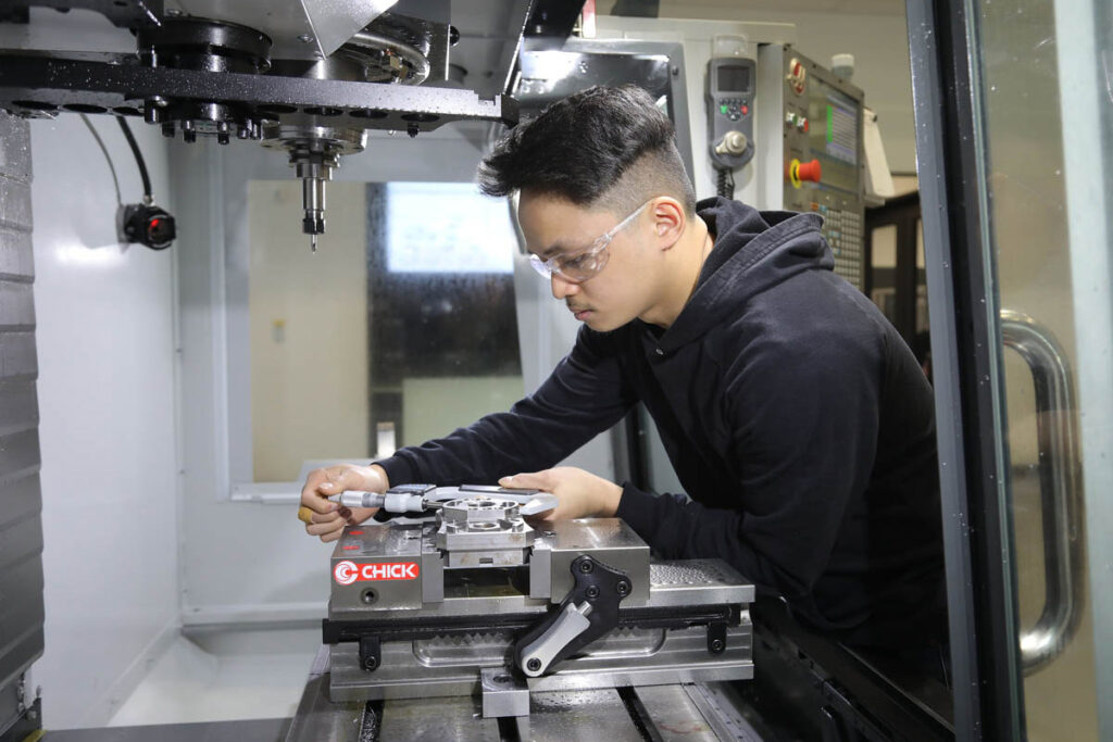 Student handing piece that is being worked by CNC machine in a lab